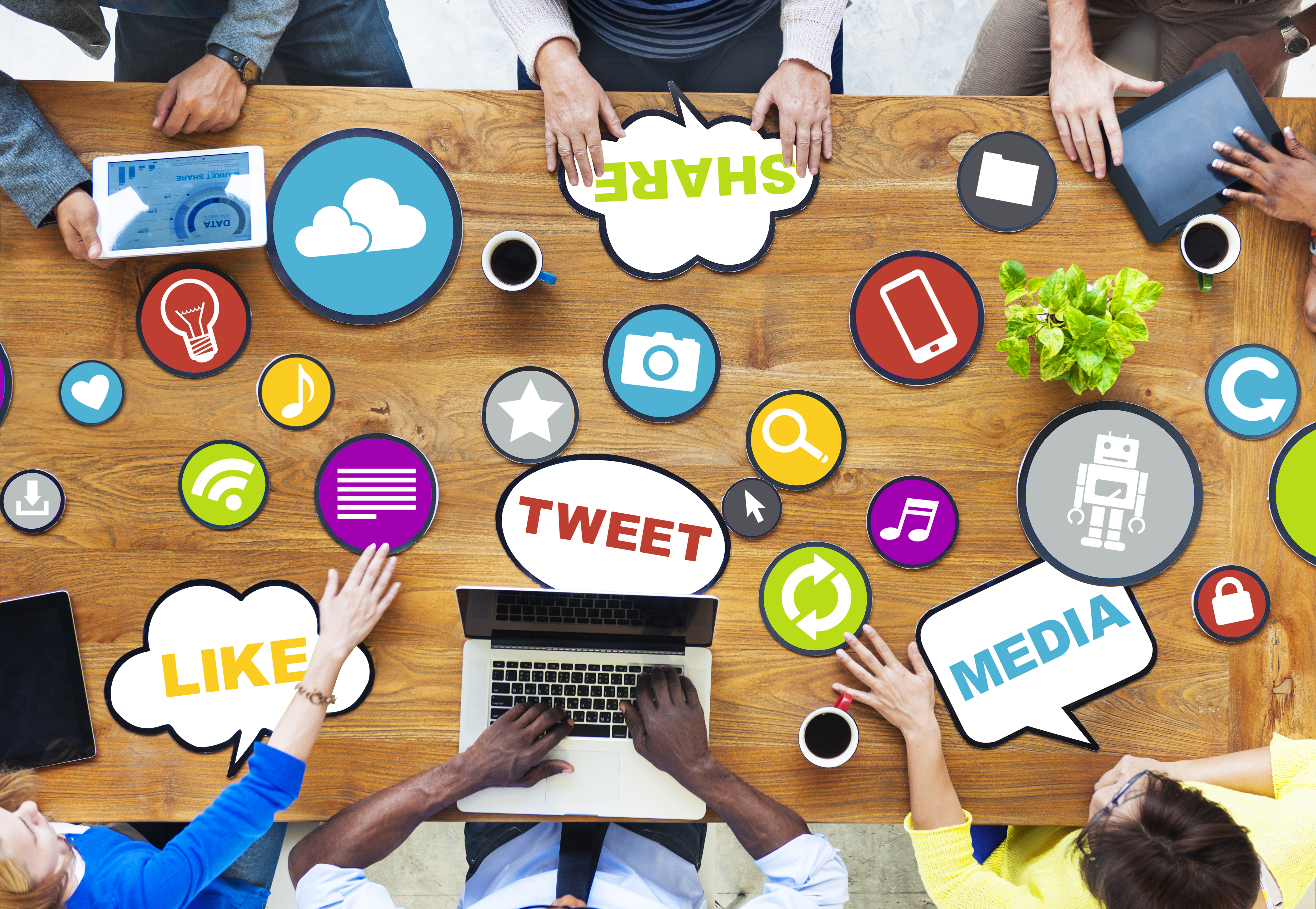 Overhead shot of 6 people around a desk with laptop and social media logos on it